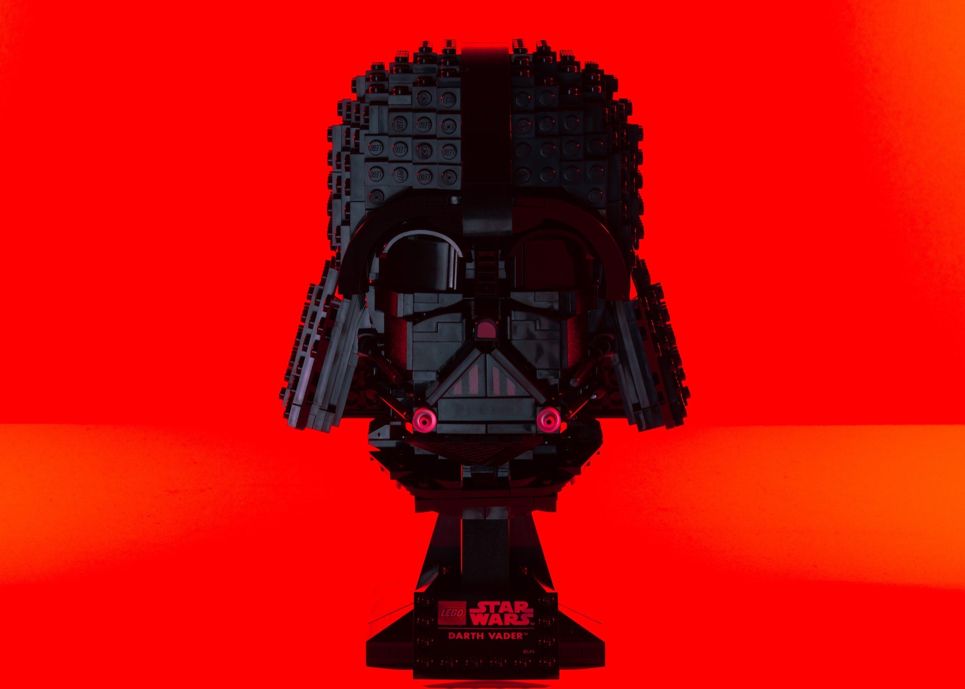 a darth vader helmet made out of lego. silhuetted against a red background.