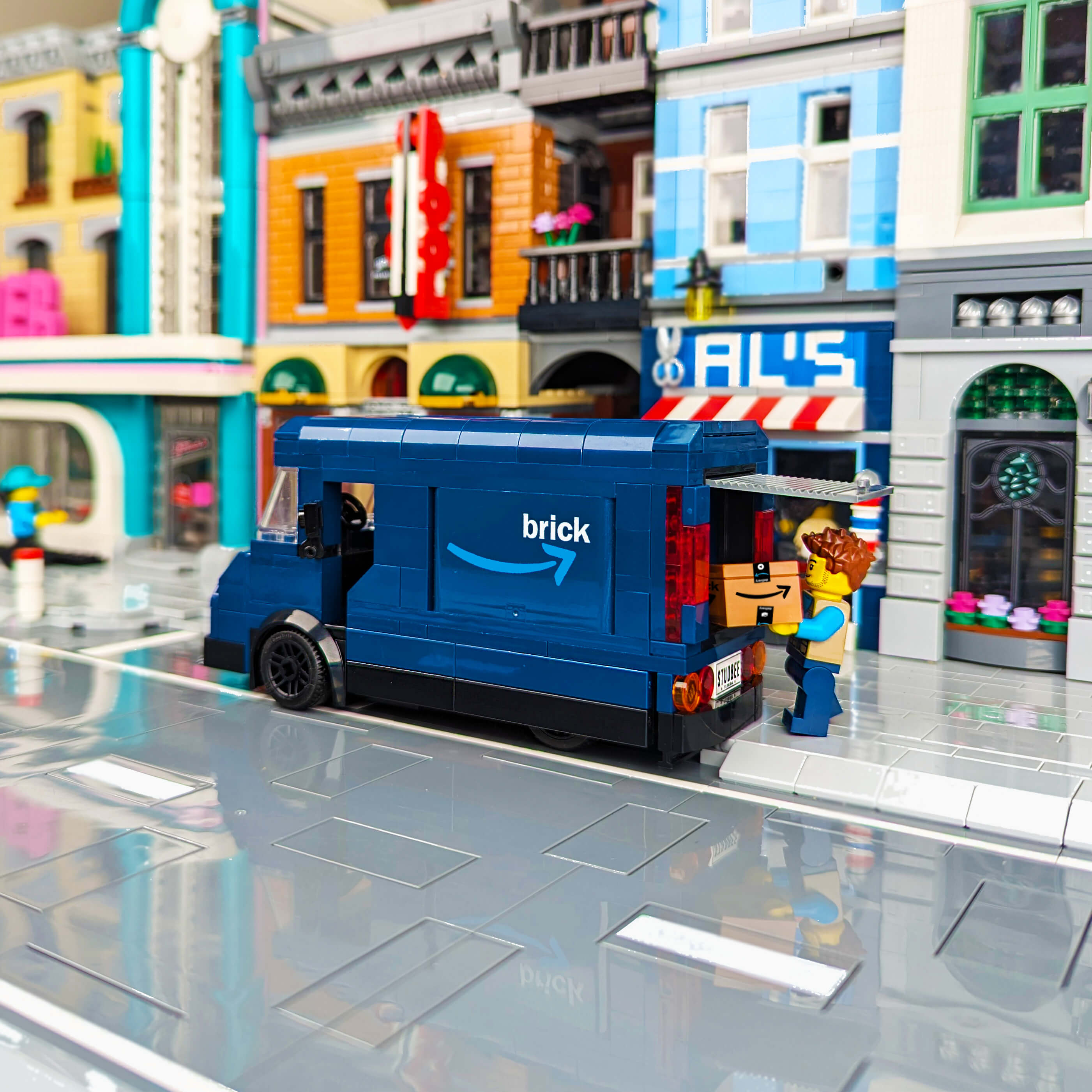 Toy Amazon delivery truck in a LEGO city street setup with buildings and a person figure.