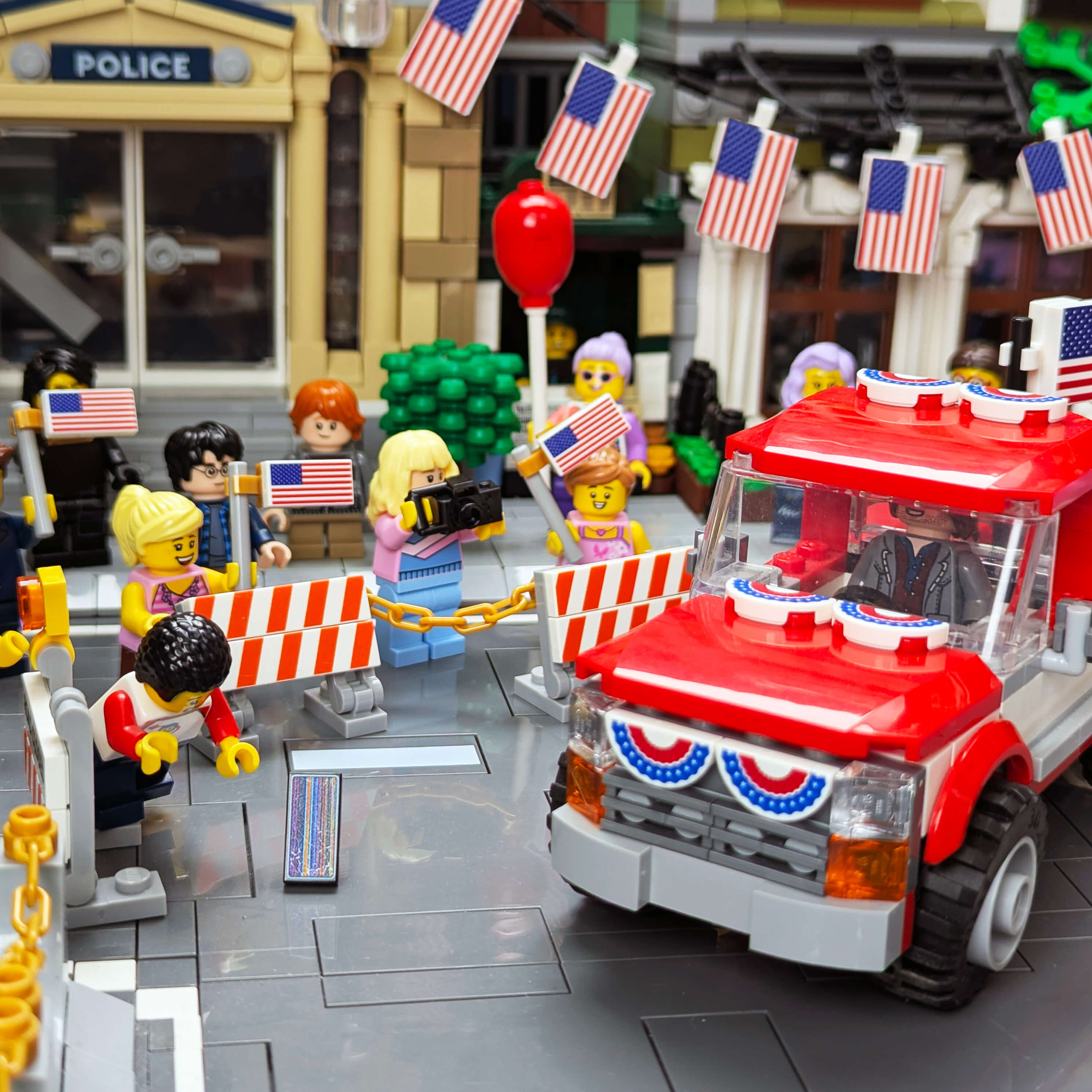 LEGO scene with a red truck, police station, and people with American flags in a town setting.