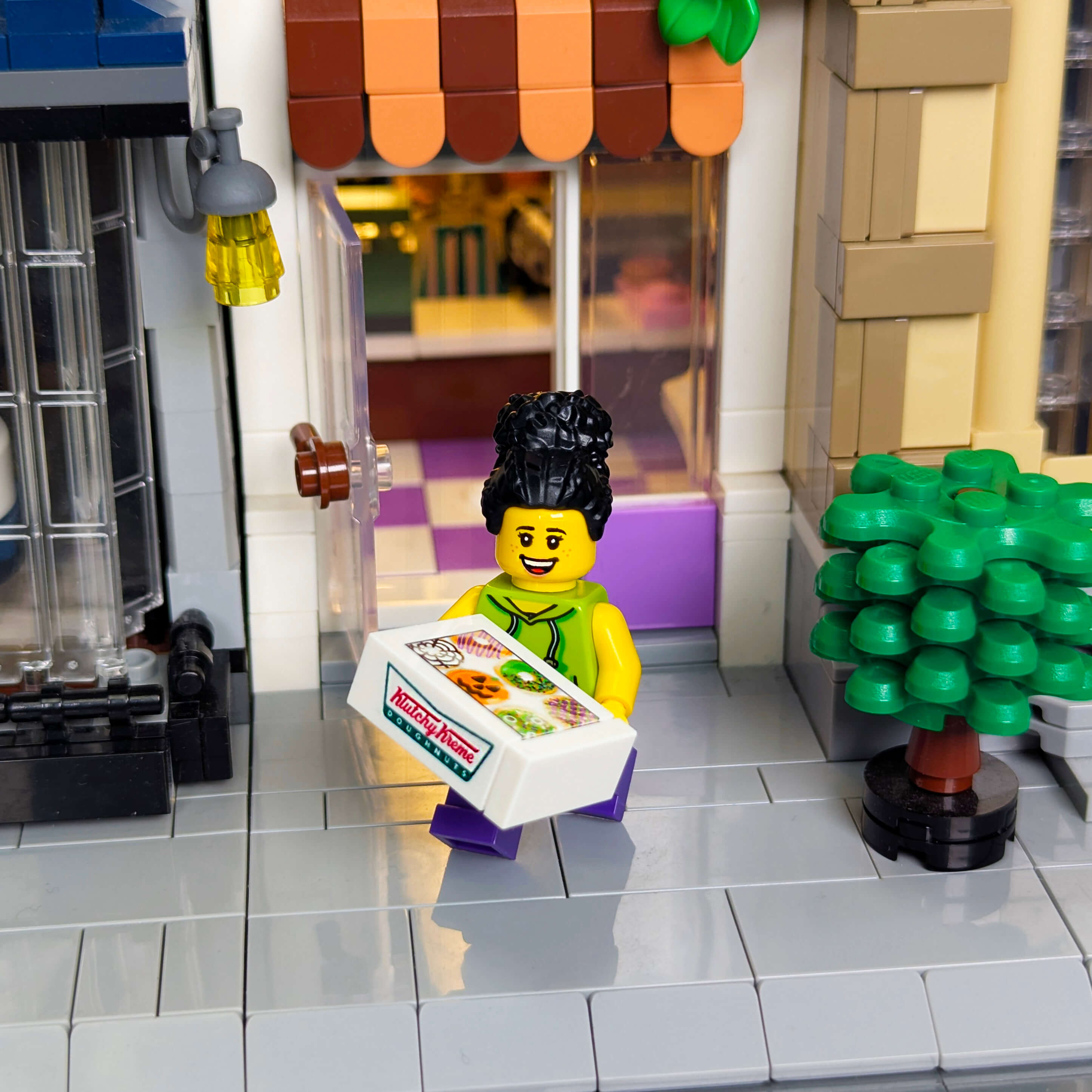 LEGO figure holding a Krispy Kreme box of Halloween donuts in front of a store. 