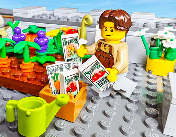 LEGO minifig of a gardener with their custom seeds and plants tending to their garden on a rooftop on a LEGO gray baseplate