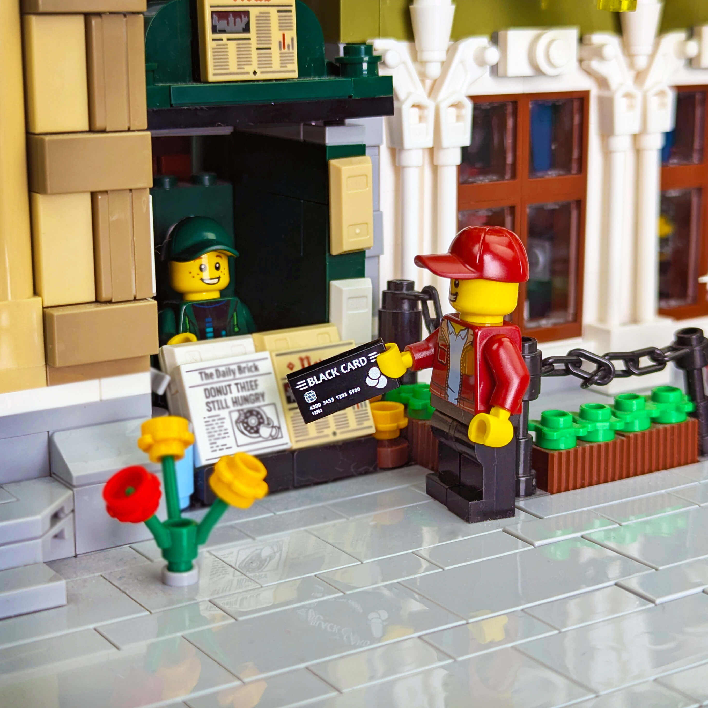 LEGO scene with a newspaper stand and characters holding a 'Black Card' in front of a building.