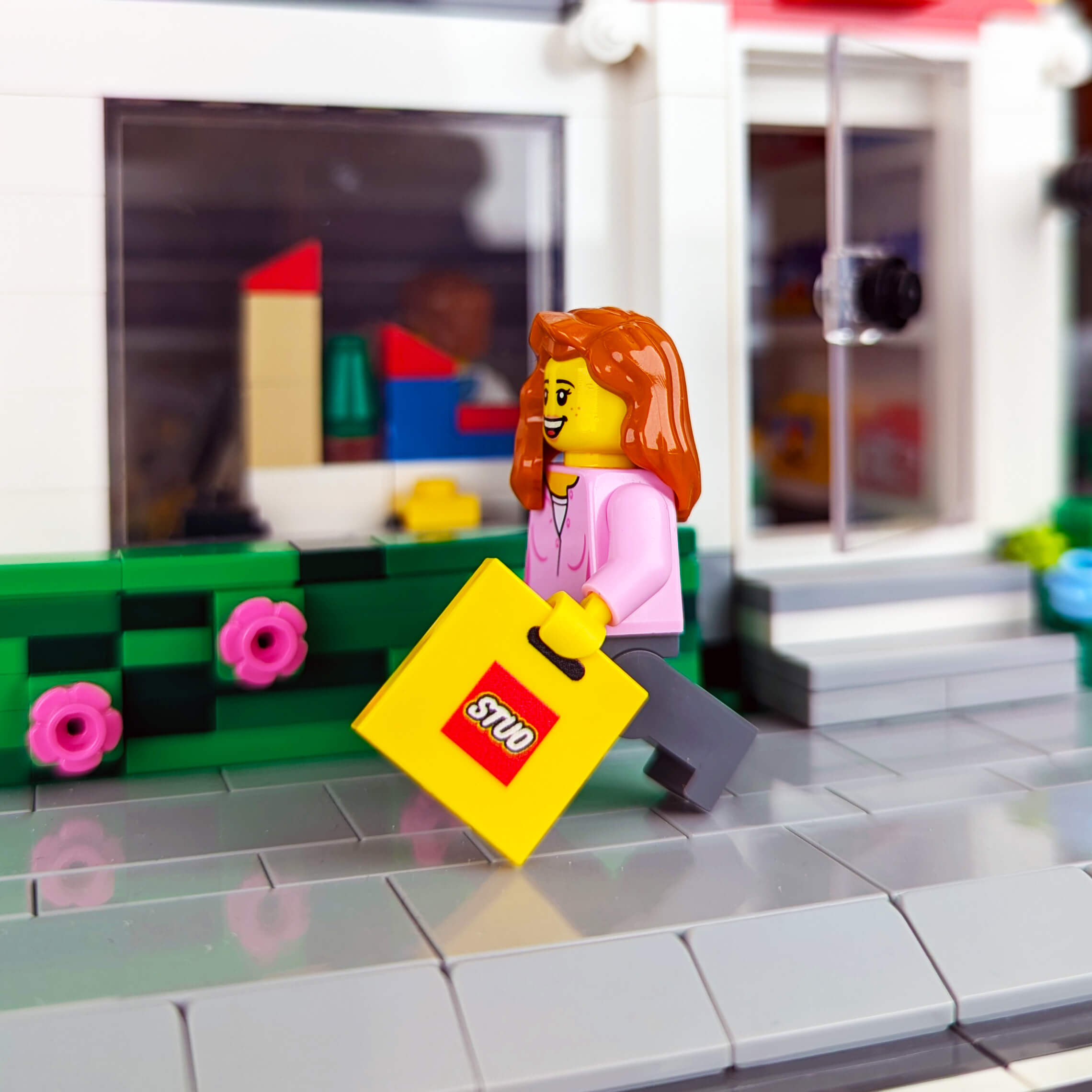 Minifig with a yellow shopping bag featuring a red 'STUD' logo in front of a store.