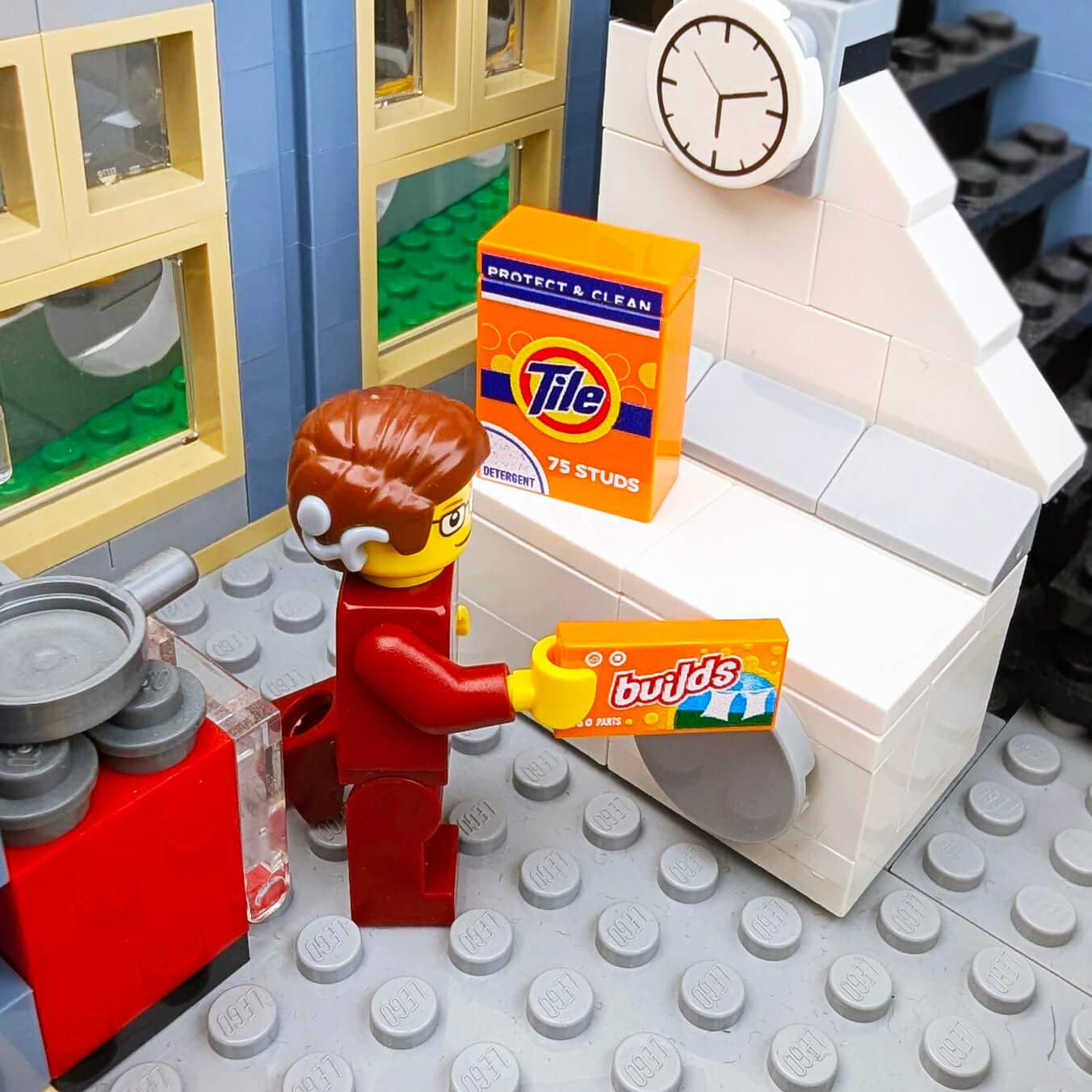 LEGO minifigure holding Tide detergent packaging in a brick built kitchen setting