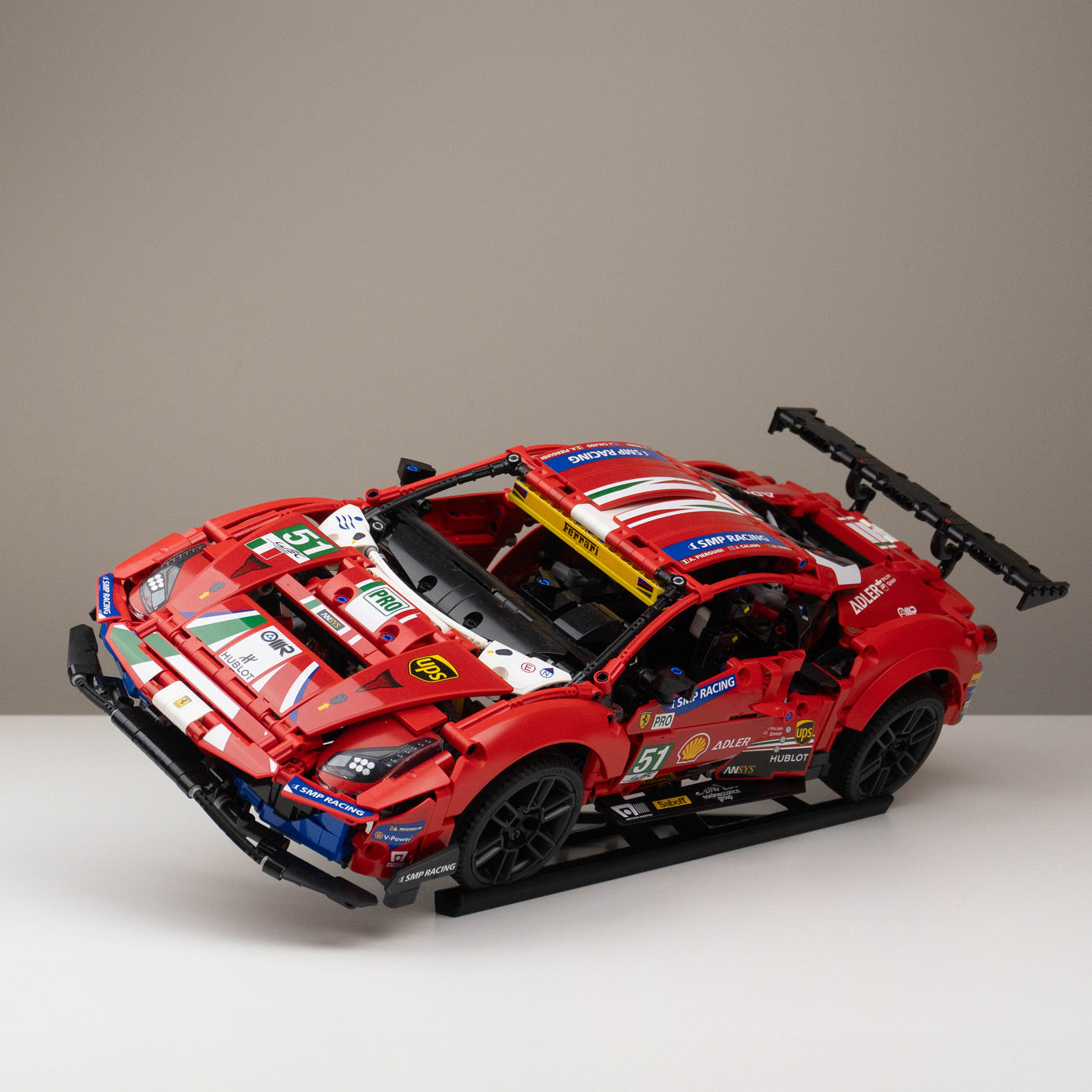 A red LEGO racing car model with detailed decals, positioned on a black stand, on a white surface.