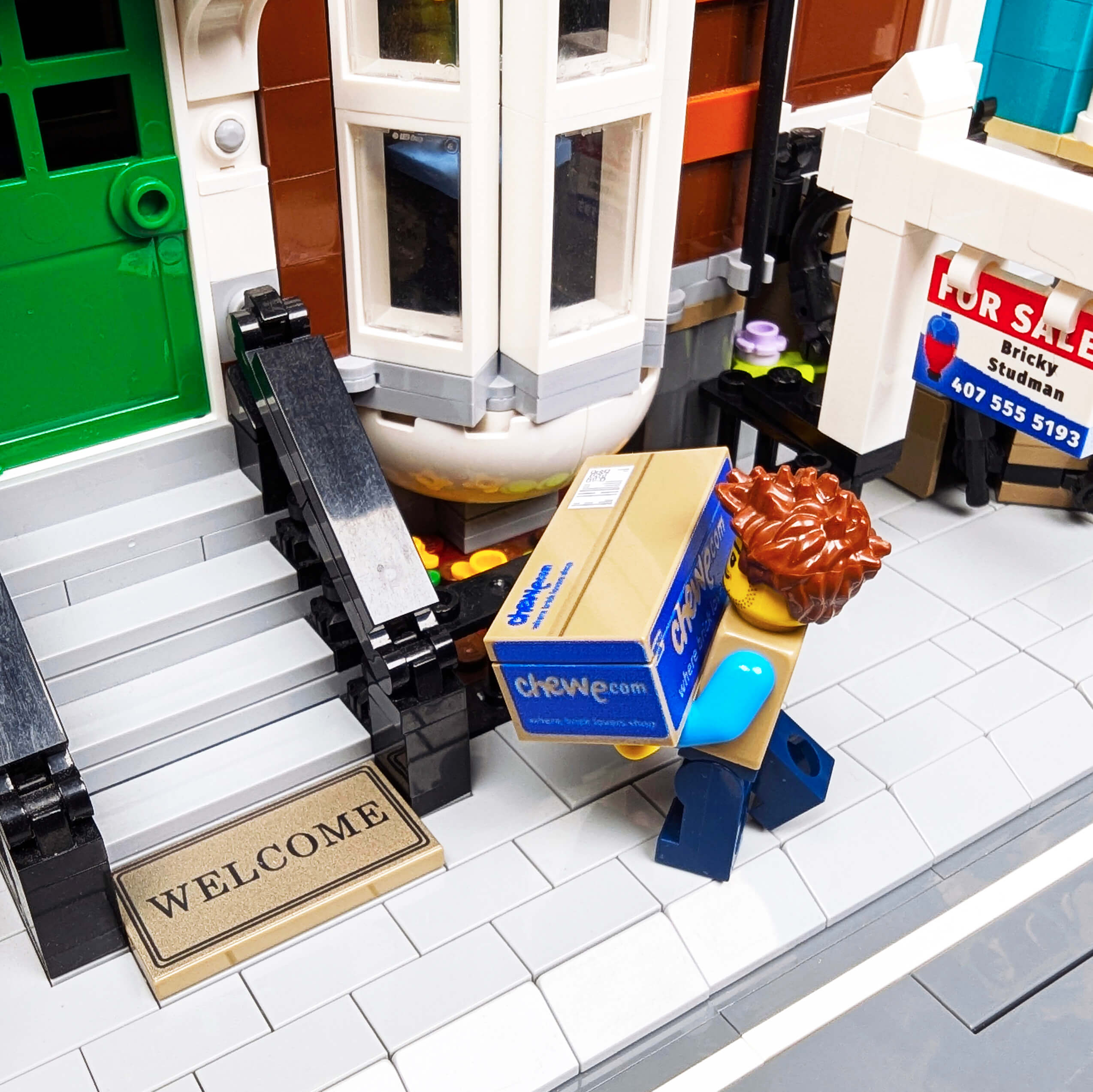 LEGO model of a door with a welcome mat, a box, and a lion figure on a tiled floor.