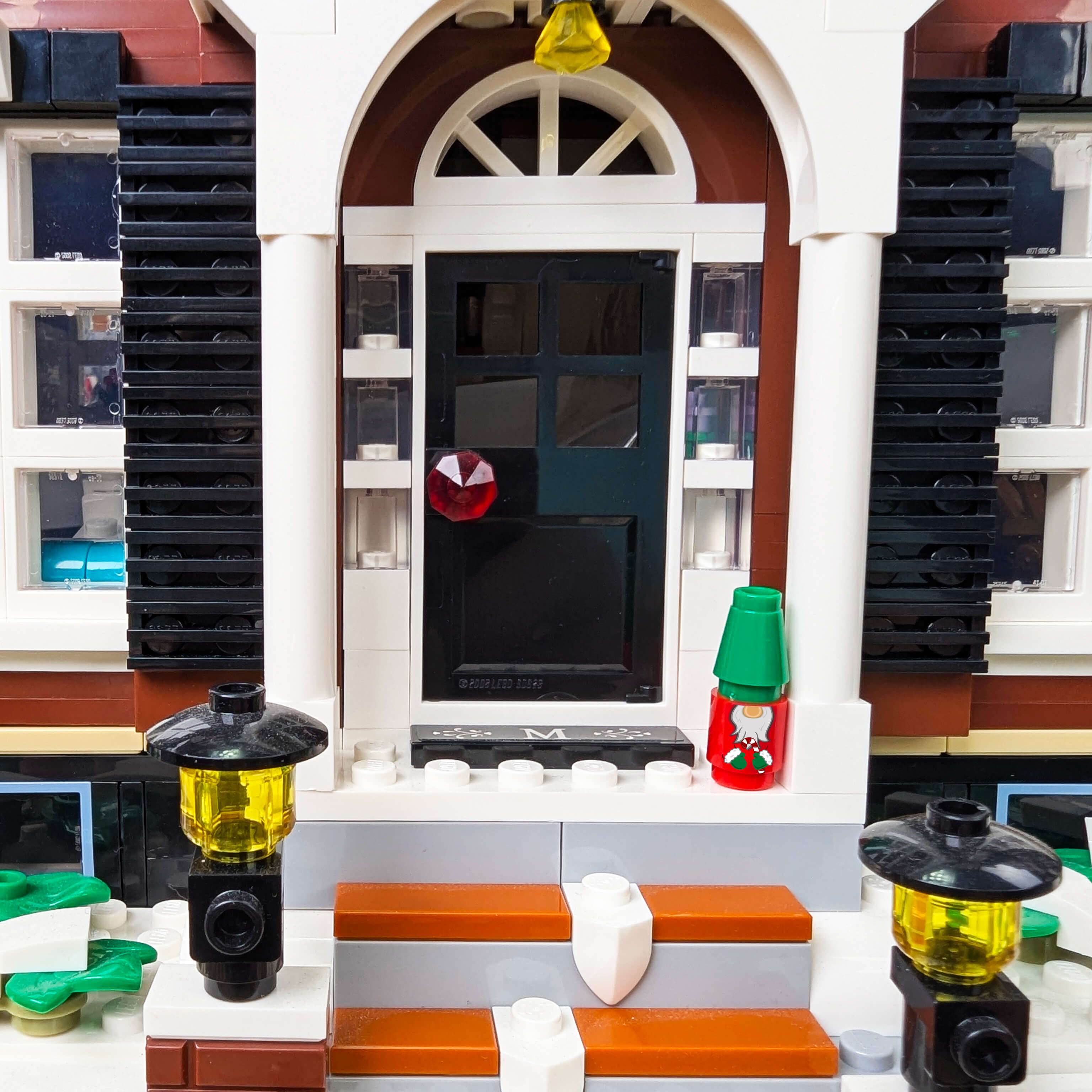 Close-up of a LEGO building with a door and windows, featuring a red and green christmas gnome on the steps.
