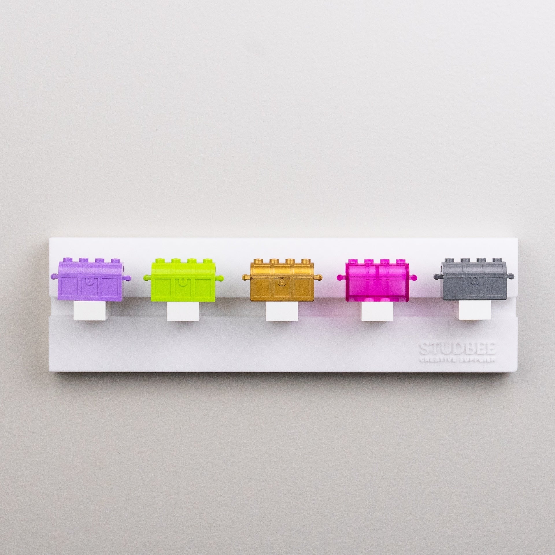 Five colorful block-like objects displayed on a single-tier white shelf with the "STUDBEE" logo.