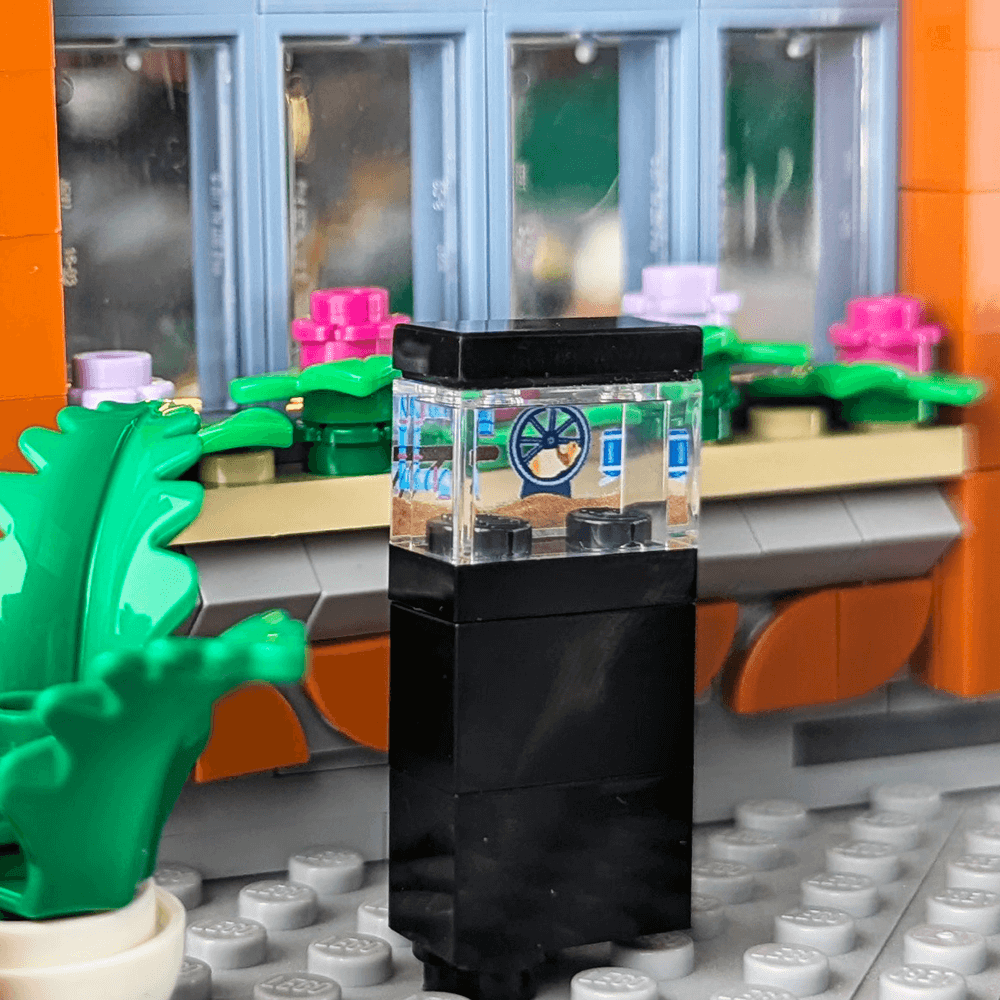 Close-up of a clear hamster enclosure made with lego bricks, with decorative plants.