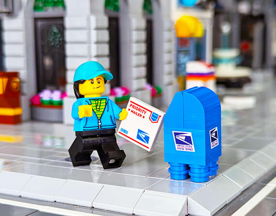LEGO minifig with a blue custom mailbox and priority mail envelope in a lego city setting