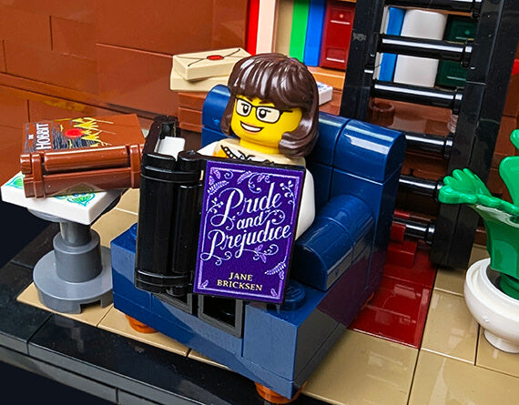LEGO minifig reading a book titled 'Pride and Prejudice' in a lego library setting with furniture and decor.