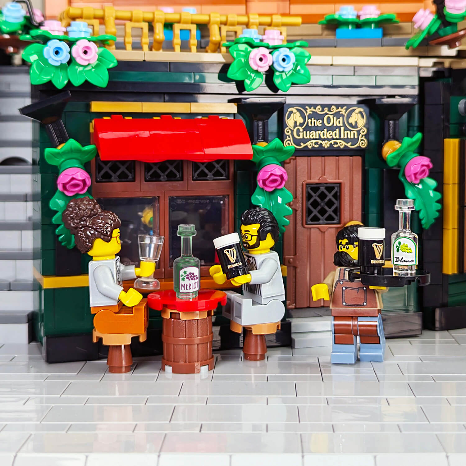 LEGO model of 'The Old Guarded Inn' with minifigs enjoying red whine and beer outside at a table.