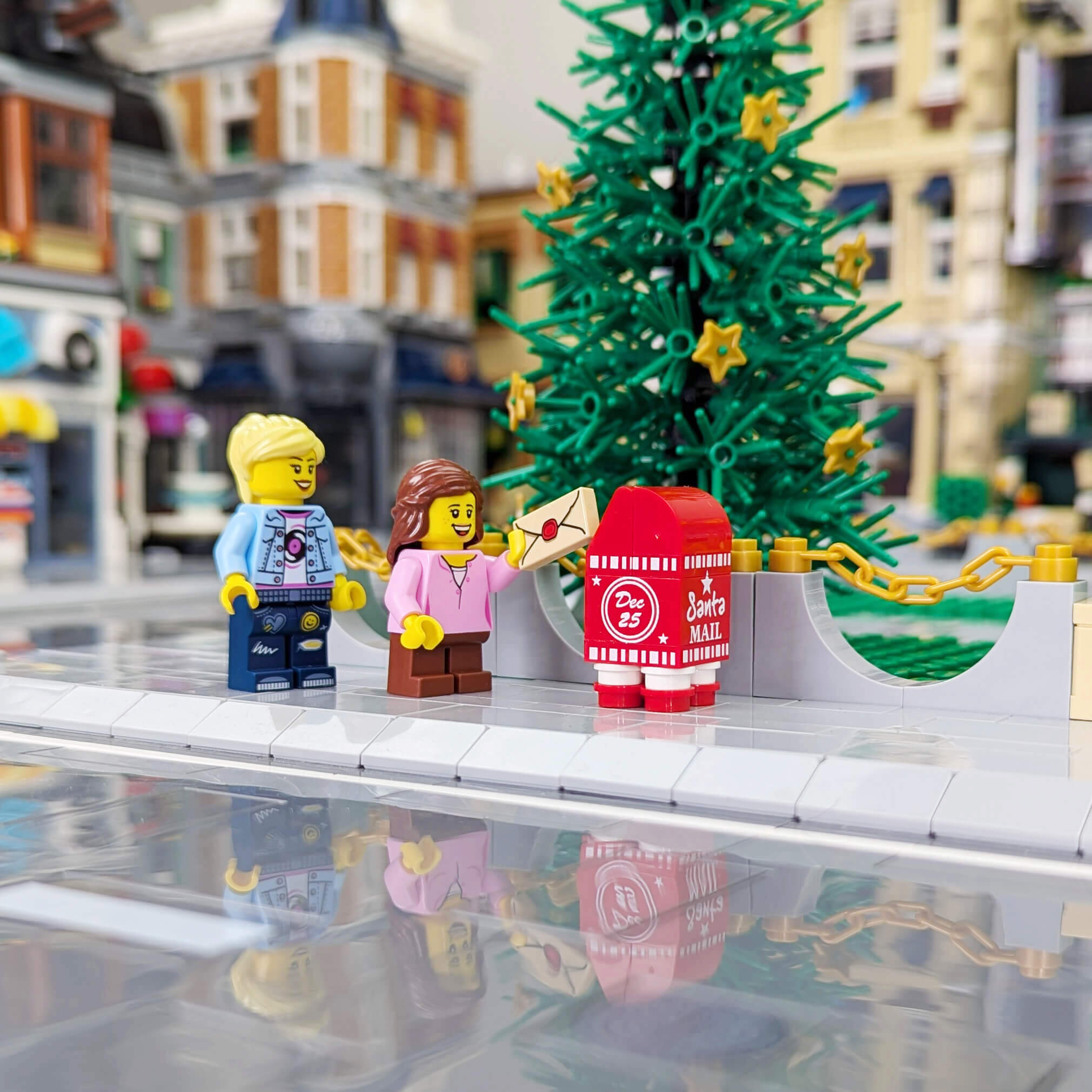 A mom and child minifigure stand next to a red LEGO mailbox that says Santa Mail on the side. 
