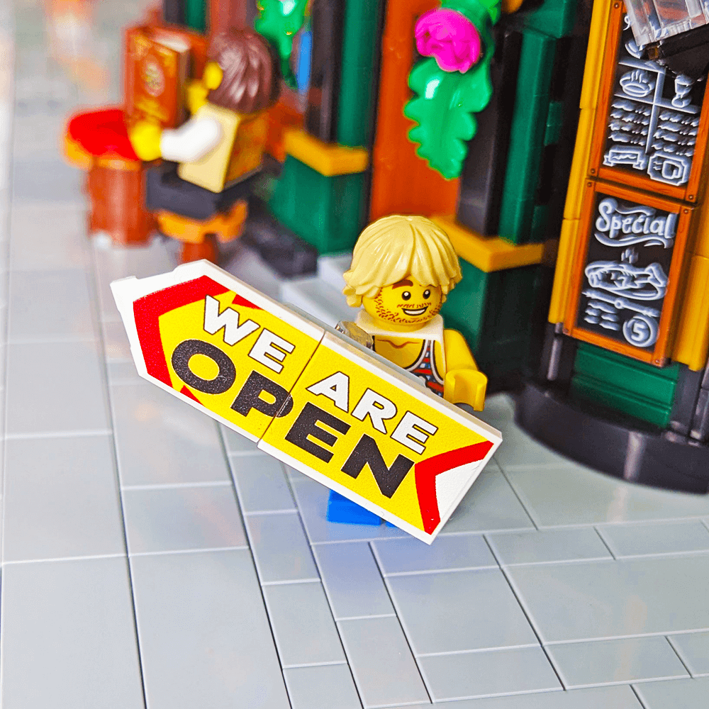 Minifigure with 'We Are Open' sign in front of a shop