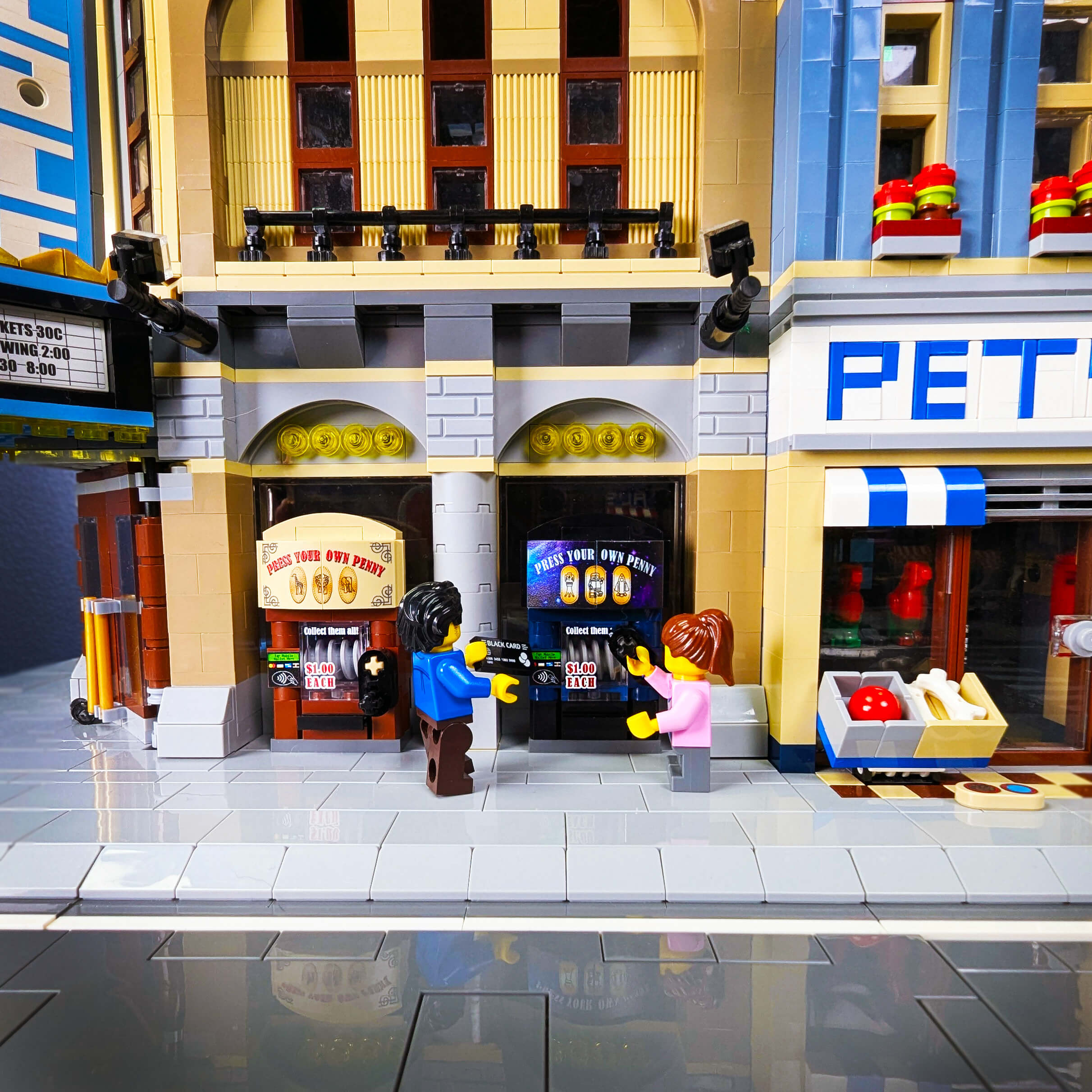 LEGO model of a city street with two minifigures buying from a penny press.