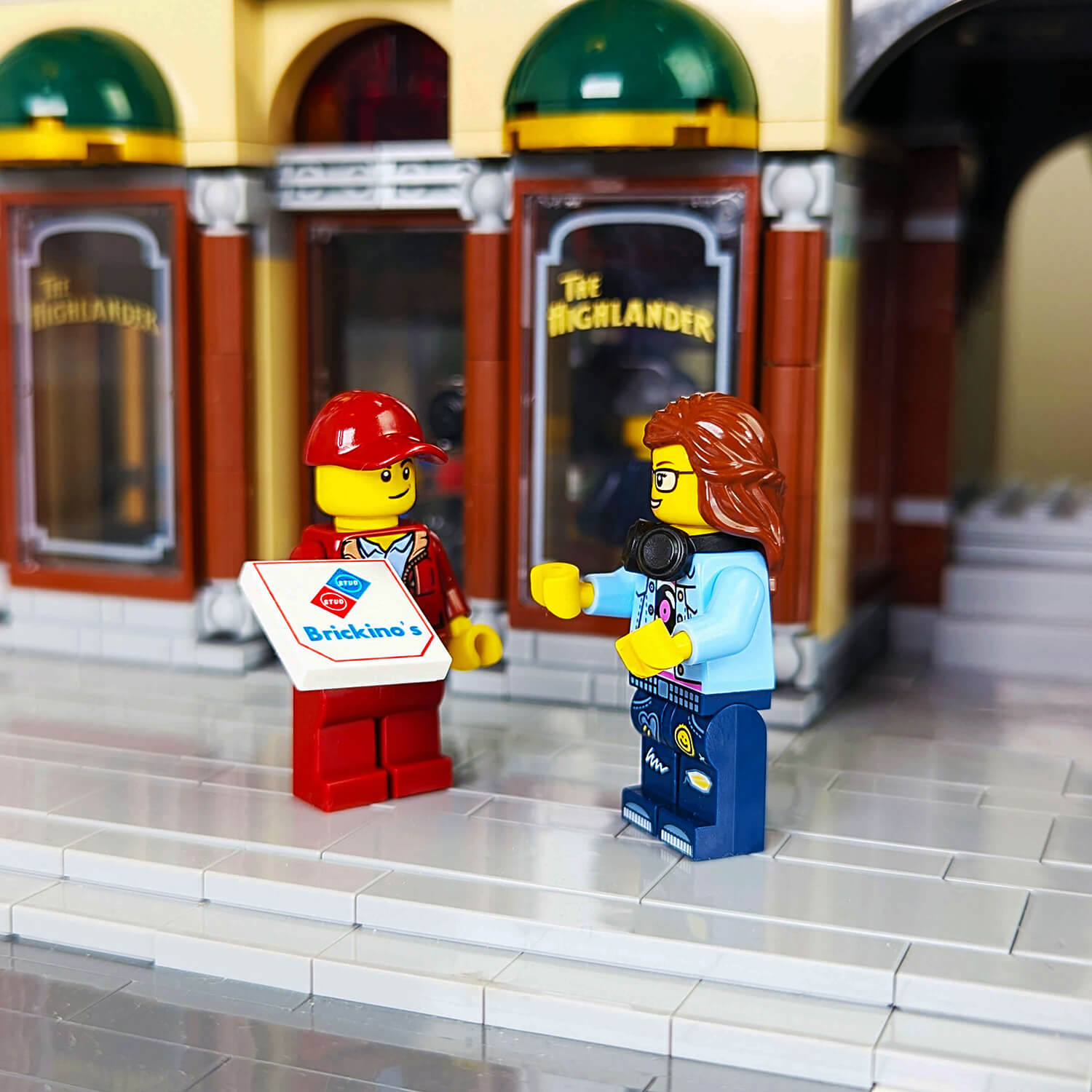 Two LEGO figures in front of a building with one holding a pizza delviery box