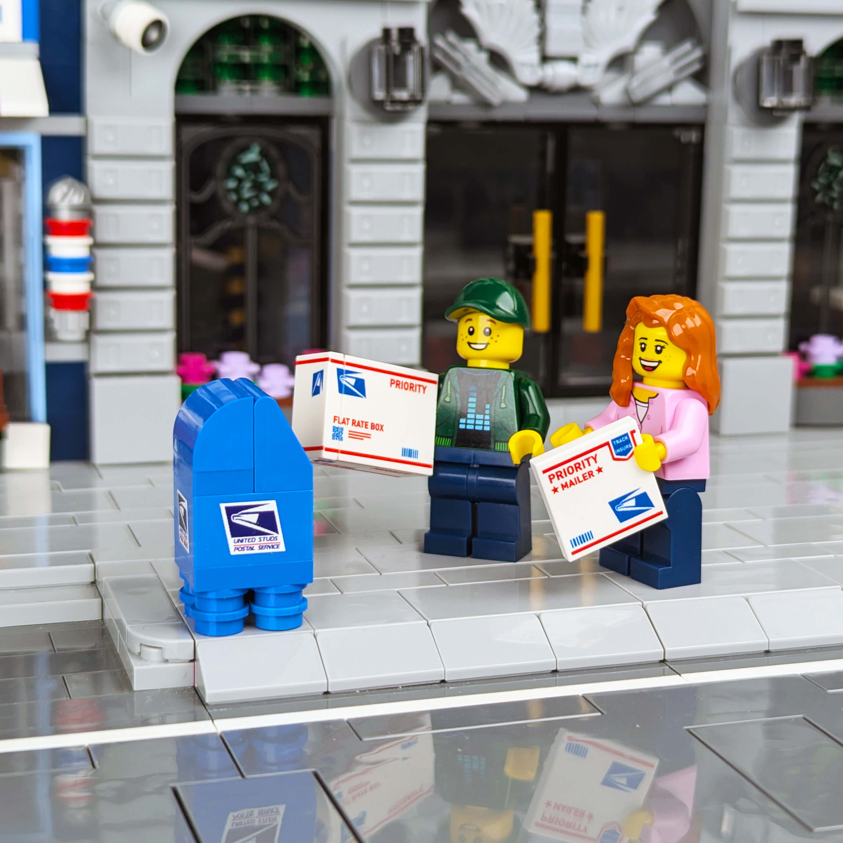 Two LEGO figures with mailboxes and envelopes in front of a store-like setting