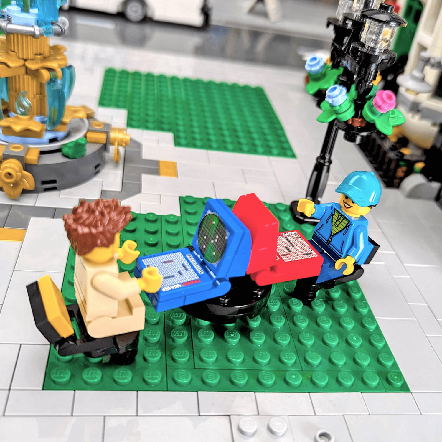 LEGO minifigs playing battleships on a green baseplate, surrounded by other LEGO structures.