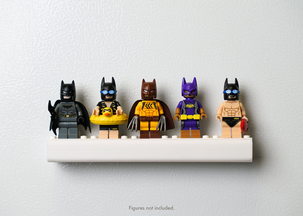 five lego batman minifigures with different costumes displayed on a magnetic shelf